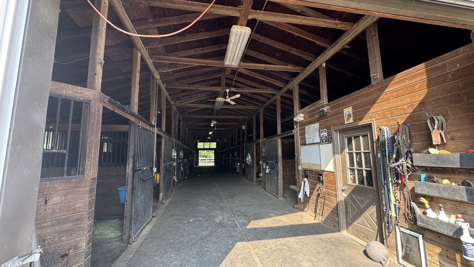 The main barn aisle at Nearaway Farm, matted underfoot, with stall fronts down both sides and daylight at the far end